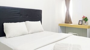 Ein ordentlich bezogenes Bett mit weißen Leinen und einem dunklen Kopfteil, ein kleiner Tisch mit einem Blumenstrauß und ein Fenster mit Vorhängen.