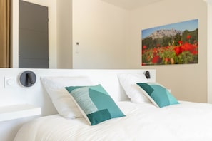 A bed with white bedding and teal pillows, a wall-mounted light, and a framed picture of a mountain landscape. - Mas de l'Etoile - Exceptional villa in Provence (Mimet)