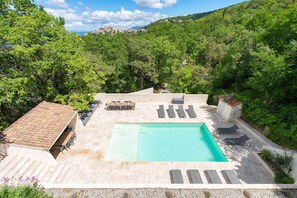 A rooftop pool with lounge chairs, a small building with a tiled roof, and a view of a hillside with trees and buildings. - Mas de l'Etoile - Exceptional villa in Provence (Mimet)