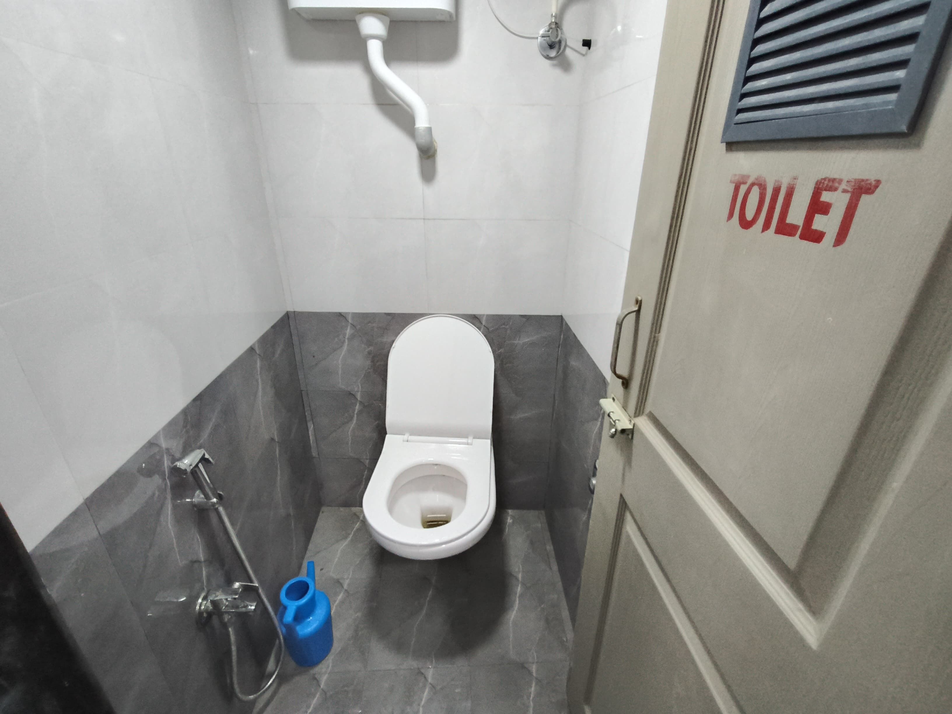 Un baño pequeño y moderno con inodoro blanco, un bidé azul y un cabezal de ducha.