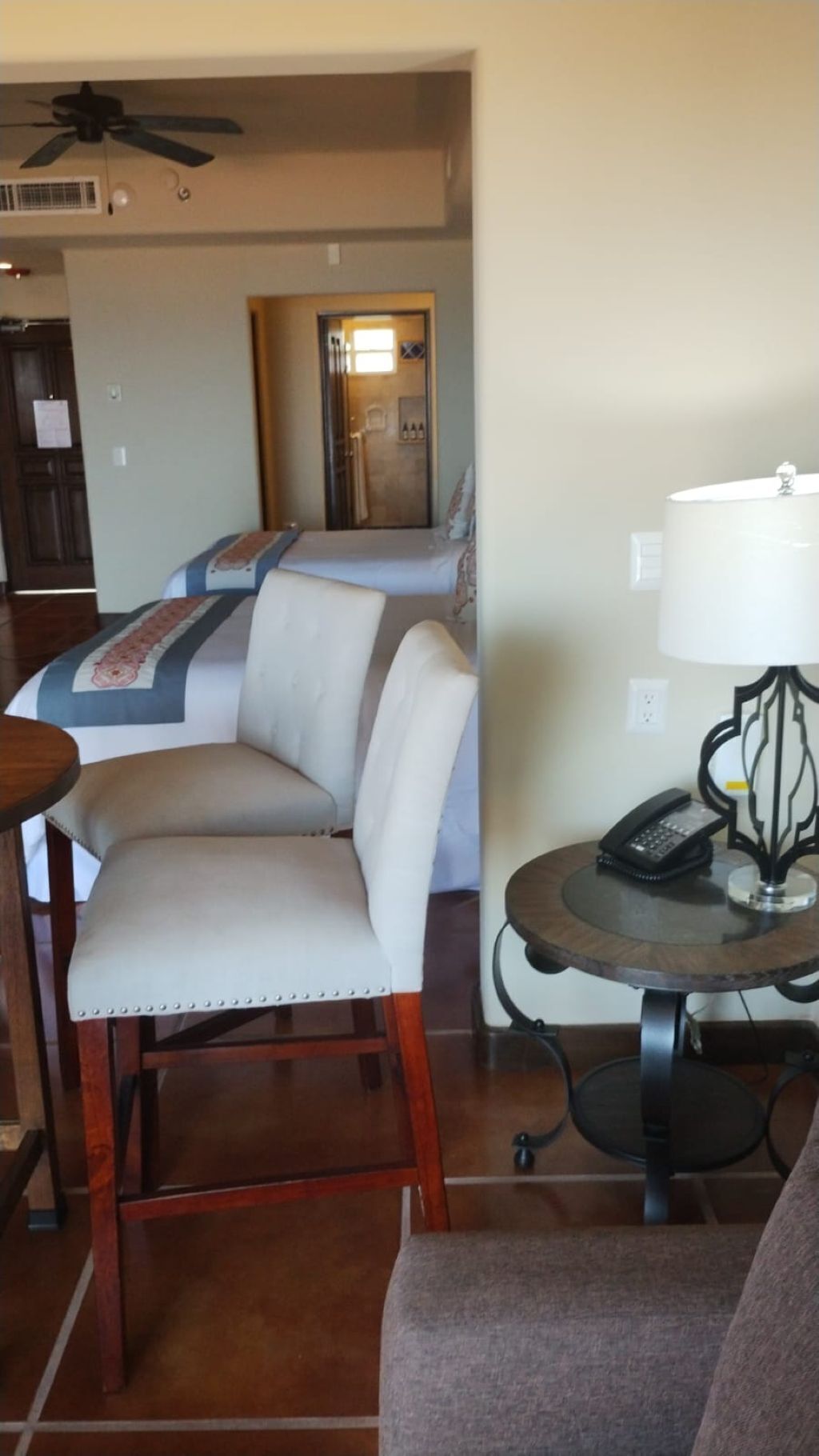 Una habitación de hotel con cama, una silla, una mesa con lámpara y un teléfono.