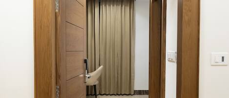 Un couloir avec un cadre de porte en bois, un interrupteur et une chaise au fond.