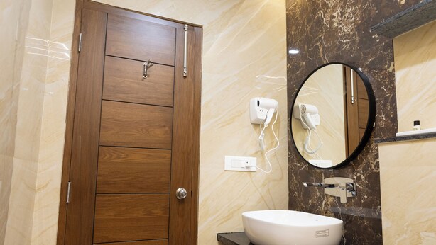 Een badkamer met een houten deur, een ronde spiegel, een witte wastafel en een haardroger aan de muur.