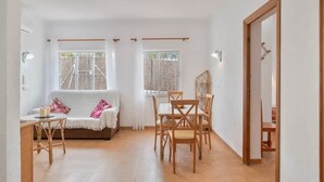 Ett ljust och luftigt vardagsrum med öppen planlösning, komplett med soffa, matbord och stolar. Det finns fönster med gardiner, en dörr och utsikt över omgivningen.