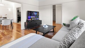 Ein modernes Wohnzimmer mit einer Couch, einem Couchtisch, einem Fernseher und einem Essbereich mit Stühlen und einem Tisch.