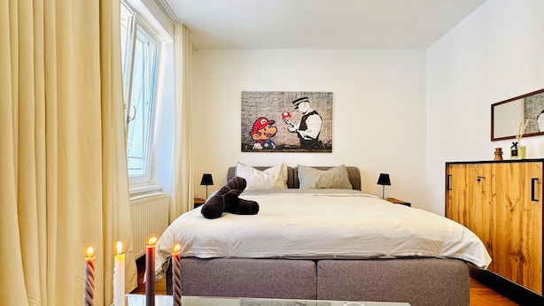 A modern bedroom with a large bed, a glass table with plates and candles, and a painting on the wall. - Comfortable Room Near Kaufpark Alterlaa (Vienna)