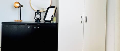 Una habitación con un aparador negro, un armario blanco, un espejo redondo y una lámpara pequeña.