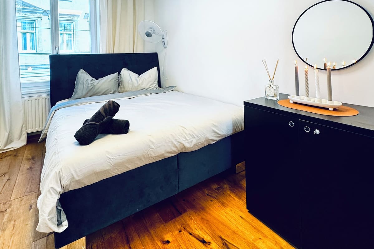 A modern bedroom with a bed, bedside table, and a mirror.
