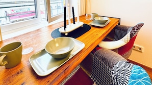 A modern dining area with a wooden table, white plates, and a view of a building through a large window. - Comfortable Room Near Kaufpark Alterlaa (Vienna)
