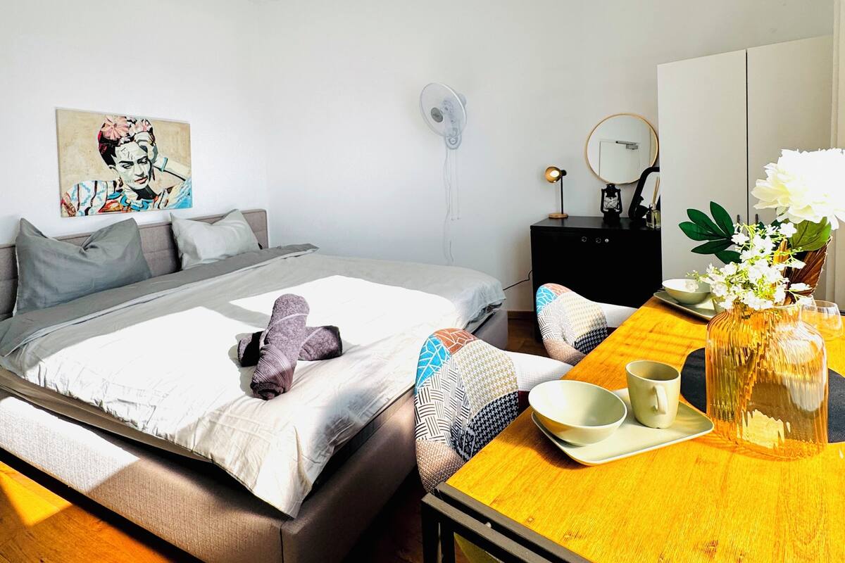 A modern bedroom with a bed, bedside table, and a small table with a vase and flowers.