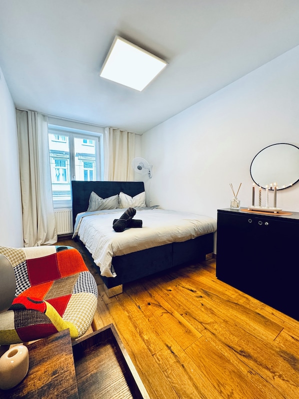 Un dormitorio moderno con cama, mesita de noche y ventana con cortinas.