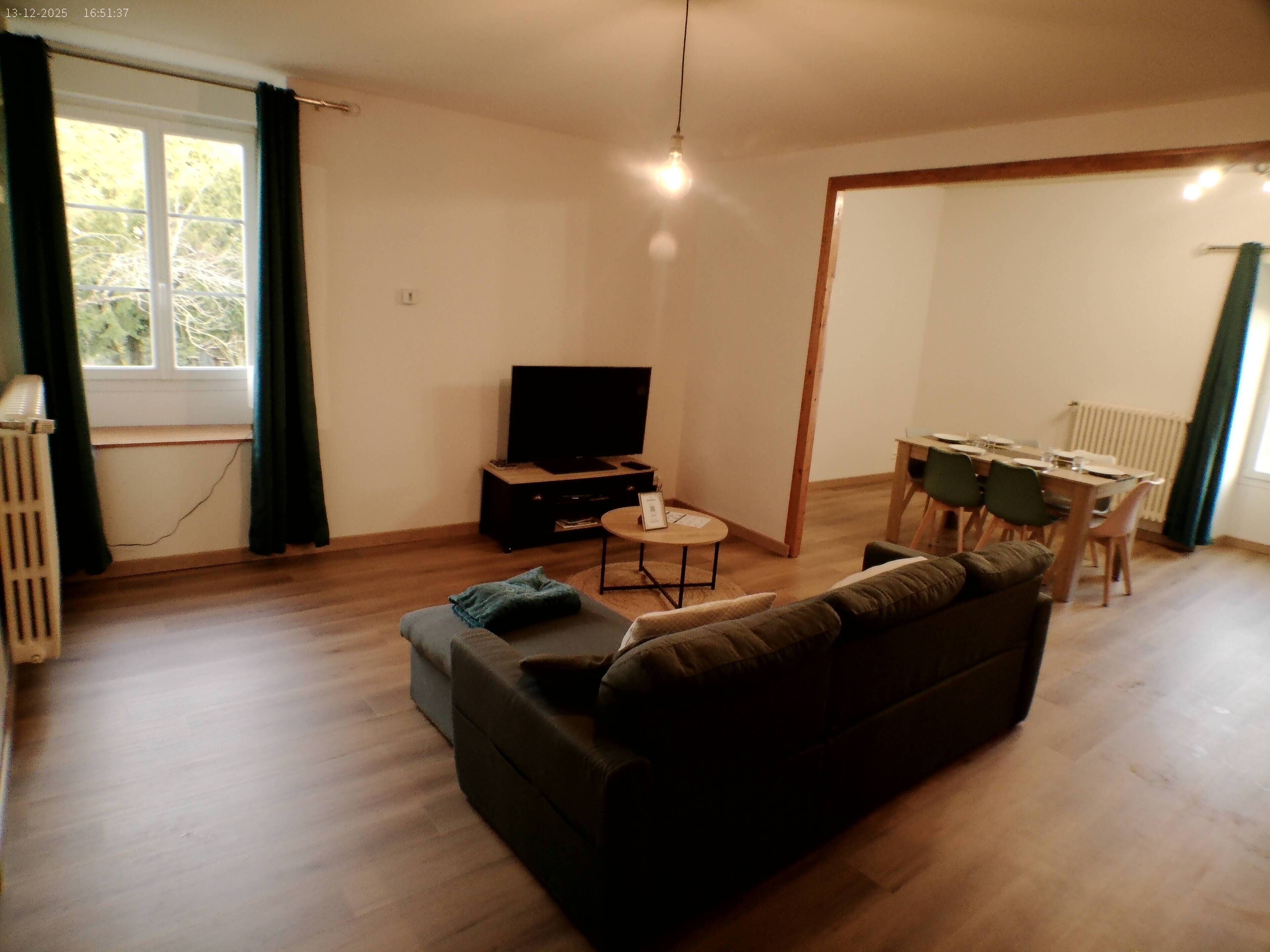 A living room with a sofa, a TV, a dining table with chairs, and a window with curtains.