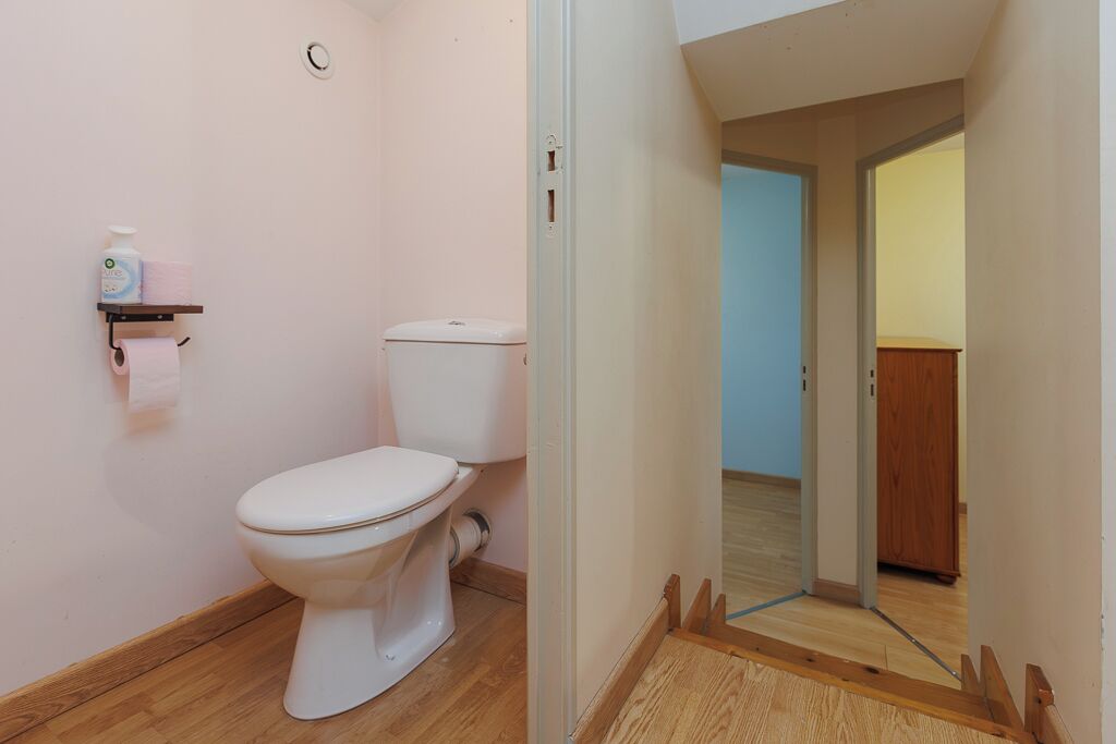 Une salle de bain avec des toilettes, une étagère contenant des articles de toilette et un plancher en bois.