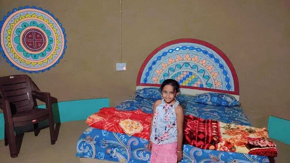 A room with a bed, a chair, and a wall with a colorful circular design. - Rann Bhagwati Home Stay (Bhuj)