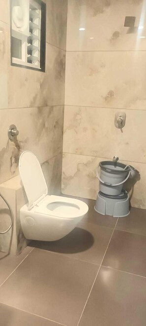 A bathroom with a white toilet, a bidet, and a marble wall. - Hotel Shiv Shakti  (Rajkot)