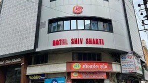 A hotel named "Hotel Shiv Shakti" with a modern architectural design, featuring a prominent sign and a storefront with various shops below. - Hotel Shiv Shakti  (Rajkot)