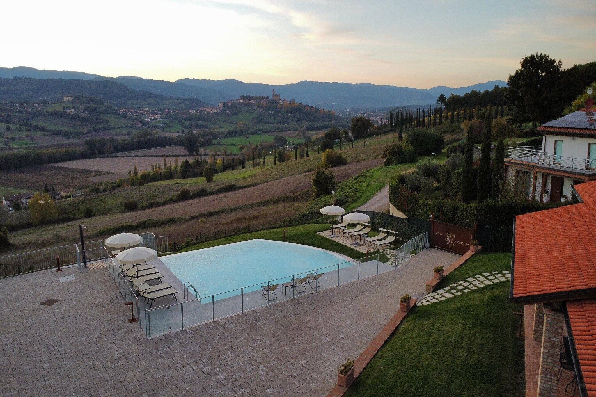 Une piscine avec des chaises longues, une terrasse dallée et une vue sur un paysage vallonné.