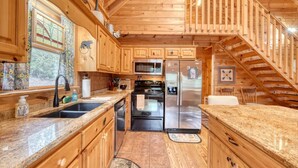 A wooden cabin kitchen with granite countertops, a stainless steel refrigerator, and a wooden staircase.
