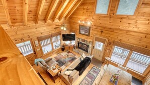 A spacious cabin with a high ceiling, wooden walls, a fireplace, and large windows.