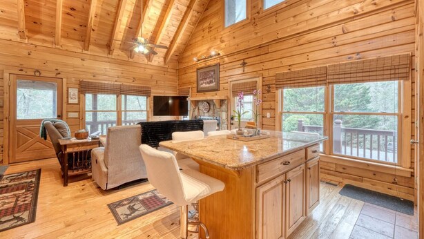 A cozy cabin interior with a kitchen, dining area, and a large window overlooking a forest.