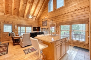 A cozy cabin interior with a kitchen, dining area, and a large window overlooking a forest. - Mountain Bearadise - Mountain views and privacy! 3 BR, 2 BA Cabin (Blairsville)