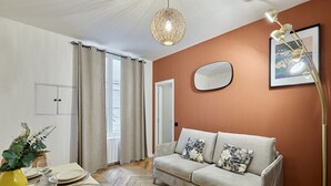 Ett modernt vardagsrum med en beige soffa, ett matbord dukat med tallrikar och glas, en hängande lampa och en inramad tavla på väggen.