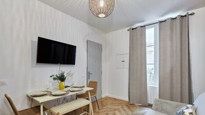 En matplats med ett bord för fyra personer, en tv som är monterad ovanför och en soffa med en kudde.