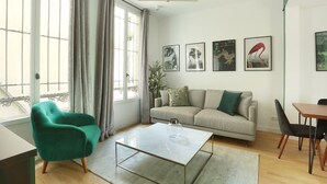 Un salon moderne comprenant un canapé, un fauteuil vert, une table basse en verre et un coin repas avec une table et des chaises.