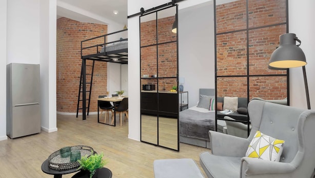 Um espaço de estar moderno com cama mezanina, área de refeições e sala de estar com sofá e poltrona.