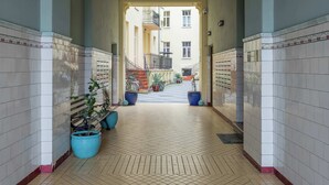 Um corredor com paredes e chão de azulejos, que leva a uma varanda com plantas em vasos e uma escadaria.