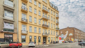 Um edifício amarelo de vários andares com varandas, uma rua em frente e um mural na lateral.