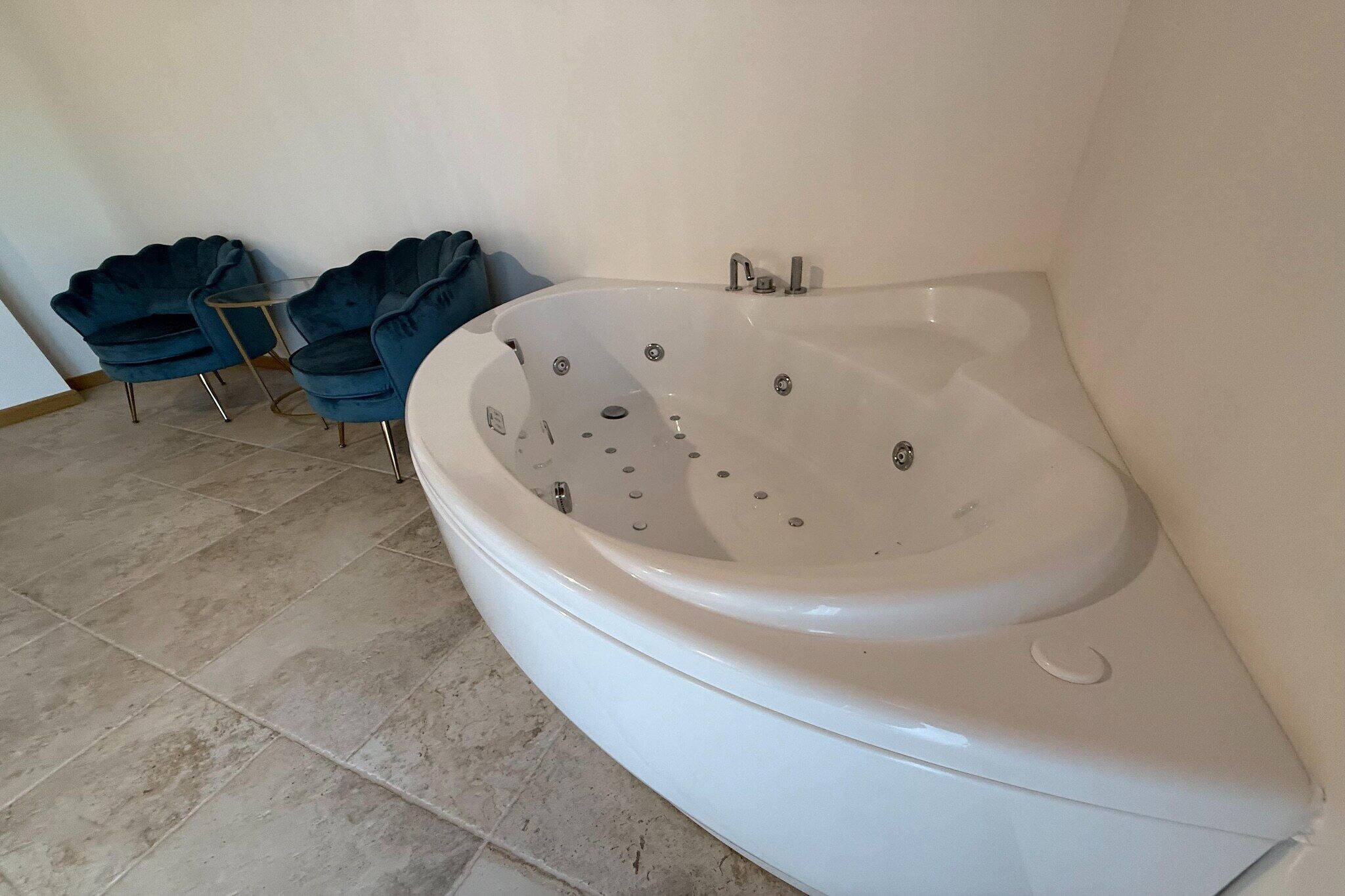 A white bathtub in a bathroom with tiled flooring and two dark blue chairs.