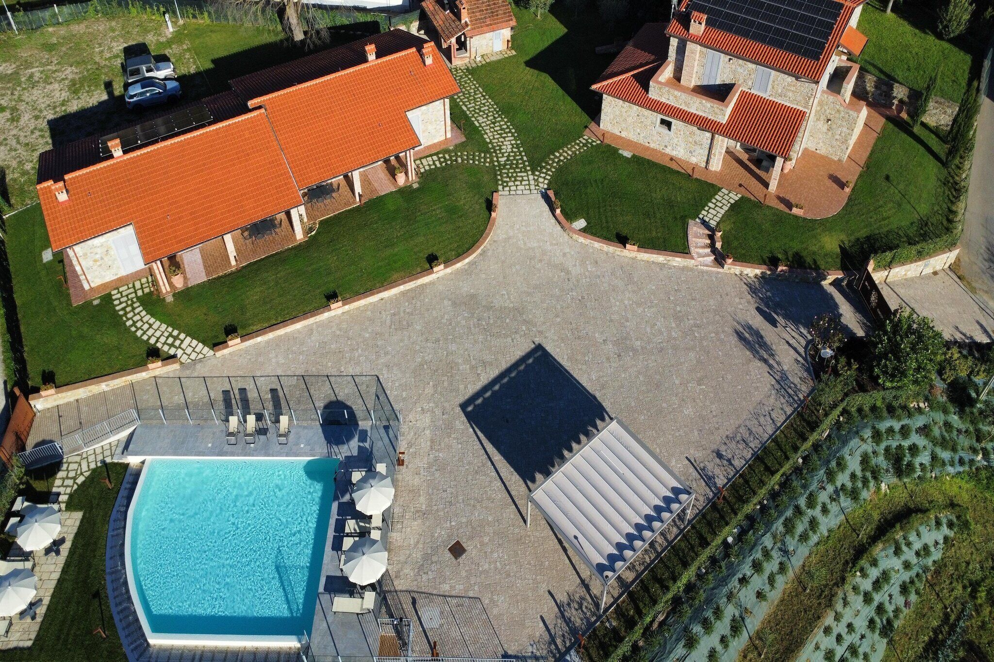 An aerial view of a property with a swimming pool, a covered outdoor area, and a landscaped garden.