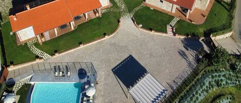 An aerial view of a property with a swimming pool, a covered outdoor area, and a landscaped garden.