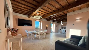 A spacious living area with a dining table, white chairs, a sofa, and a TV mounted on the wall. - Spacious apartment with infinity pool (Poppi)