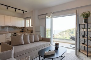A modern living room with a sofa, coffee table, and a view of a balcony with a scenic landscape. - Sky, Luxury Apartment (Rhodes)