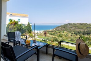 A balcony with a view of the sea, a table with a magazine, and a straw hat hanging on the railing. - Sky, Luxury Apartment (Rhodes)