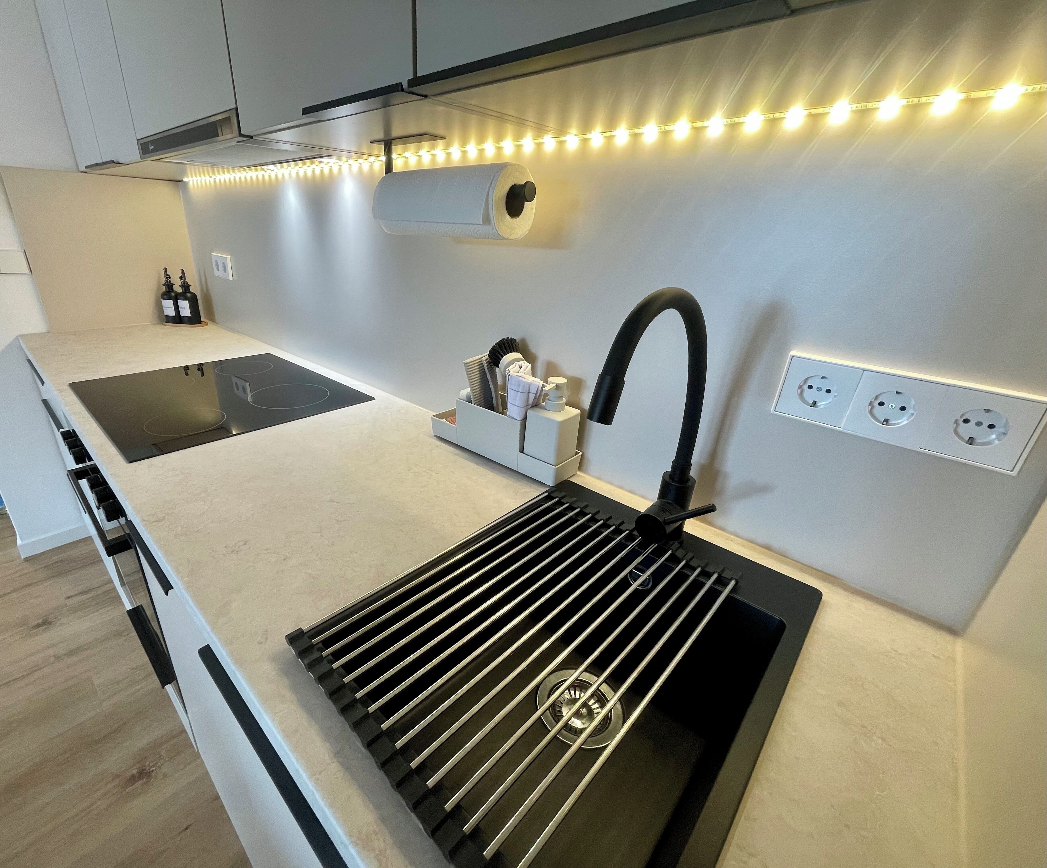 A modern kitchen with a black sink, a built-in stove, and a countertop with a paper towel holder.