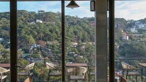 A dining area with a table and chairs, large windows offering a view of a hilly landscape. - HLS Dalat Lodge (Xuan Huong - Da Lat)