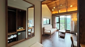 Een kamer met een houten plafond, een grote spiegel, een bank, een eettafel en uitzicht op groen buiten.
