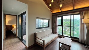 Een moderne hotelkamer met een houten plafond, een bank, een tafel en grote ramen met uitzicht op het omliggende landschap.