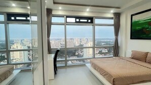 A modern bedroom with a large bed, a desk, and a view of a cityscape through large windows. - Victory Tower (Ho Chi Minh City)