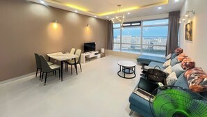 A modern living room with a dining area, a sofa set, a TV, and a large window offering a city view. - Victory Tower (Ho Chi Minh City)