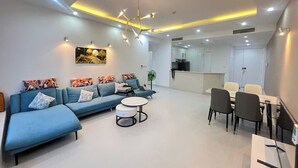 A modern living room with a blue sofa, a round coffee table, and a dining area with chairs and a table. - Victory Tower (Ho Chi Minh City)