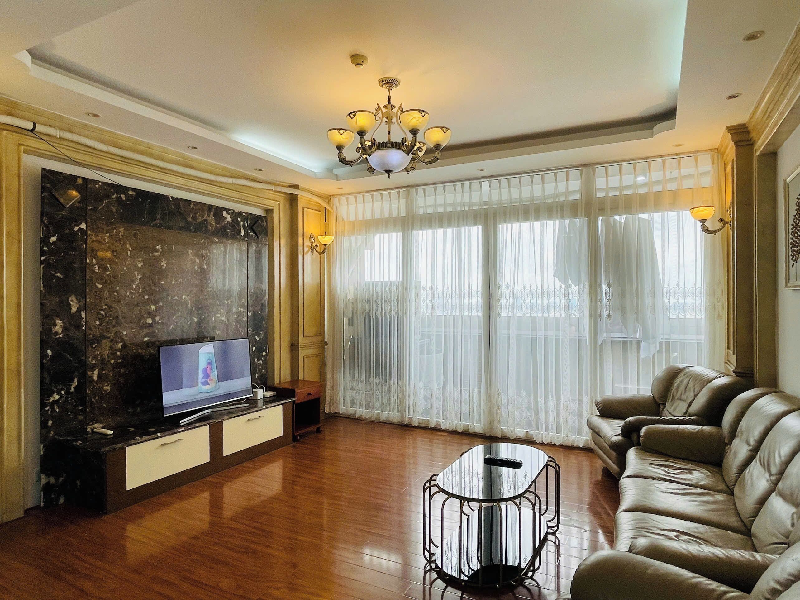 A living room with a TV, a sofa, a coffee table, and a chandelier.