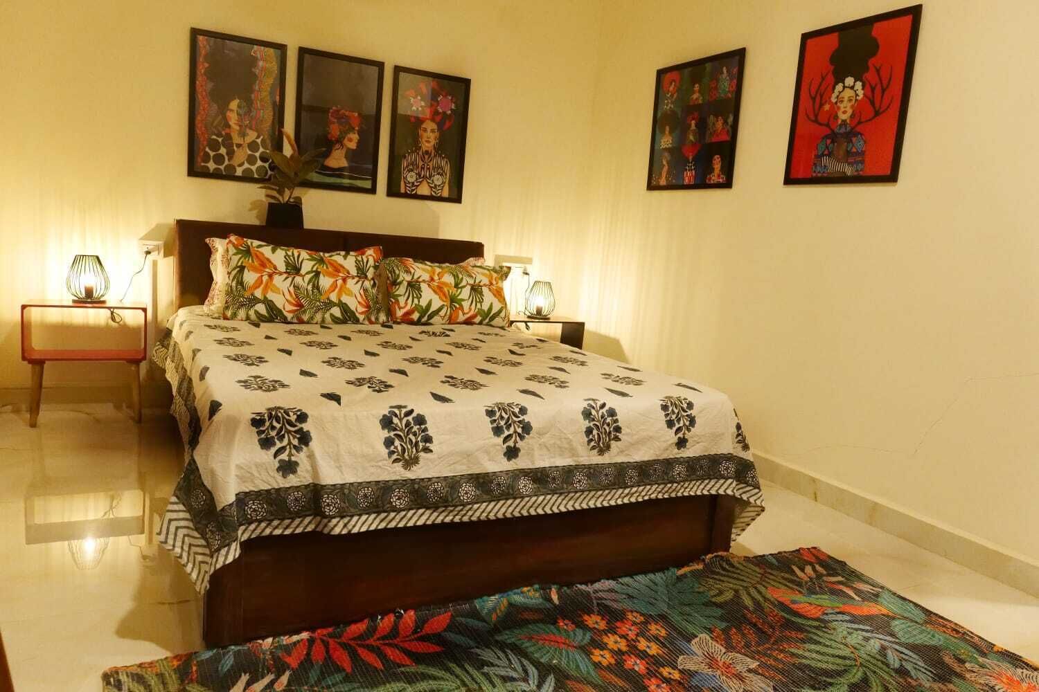 Une chambre à coucher avec un lit, deux tables de chevet et une petite table d’appoint. Trois œuvres d’art encadrées ornent le mur.