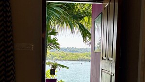 Une porte donnant sur un balcon d’où l’on peut admirer un paysage paisible, avec une étendue d’eau calme et de la verdure.