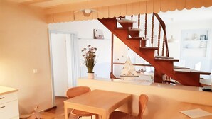 A cozy dining area with a wooden table and chairs, a small potted plant, and a staircase leading to an upper level. - Romantischer Rückzugsort in Kröpelin in Strandnähe (Kröpelin)