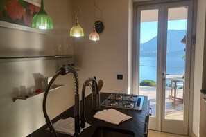 Eine Küche mit einem Gaskochfeld, einem Spülbecken mit Schlauchanschluss und Meerblick durch eine Glastür.
