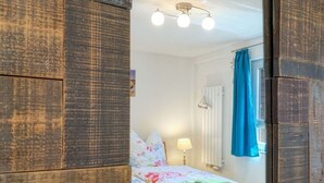 Quarto com cama, mesa de cabeceira, luminária e janela com cortinas.